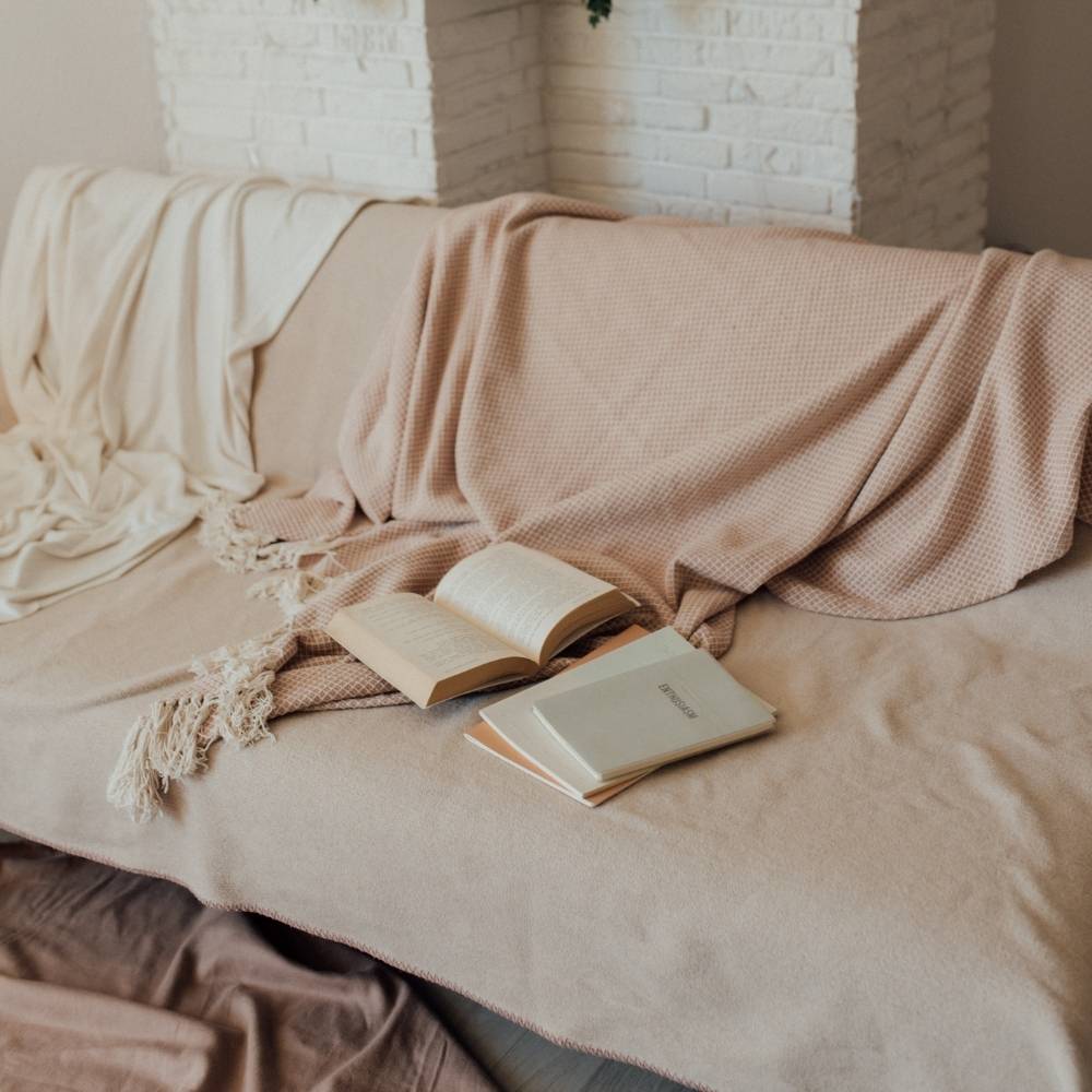 Ein Sofa mit einer beigen Decke und einer altrosa Decke mit Fransen